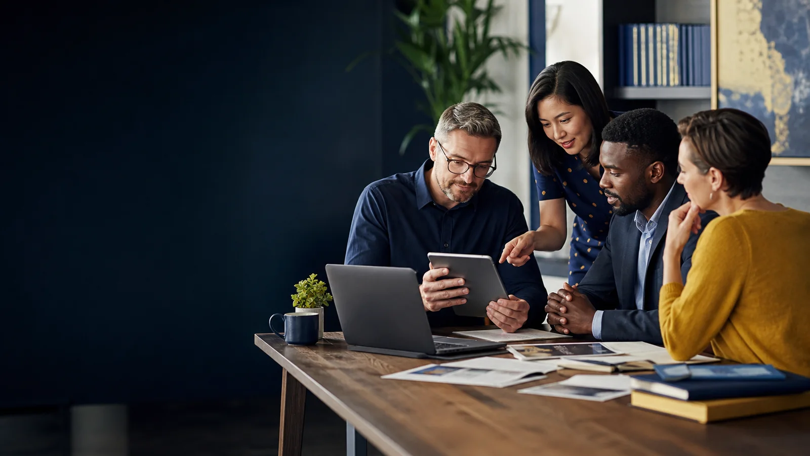 A team collaborating around laptops, a tablet, and printed documents