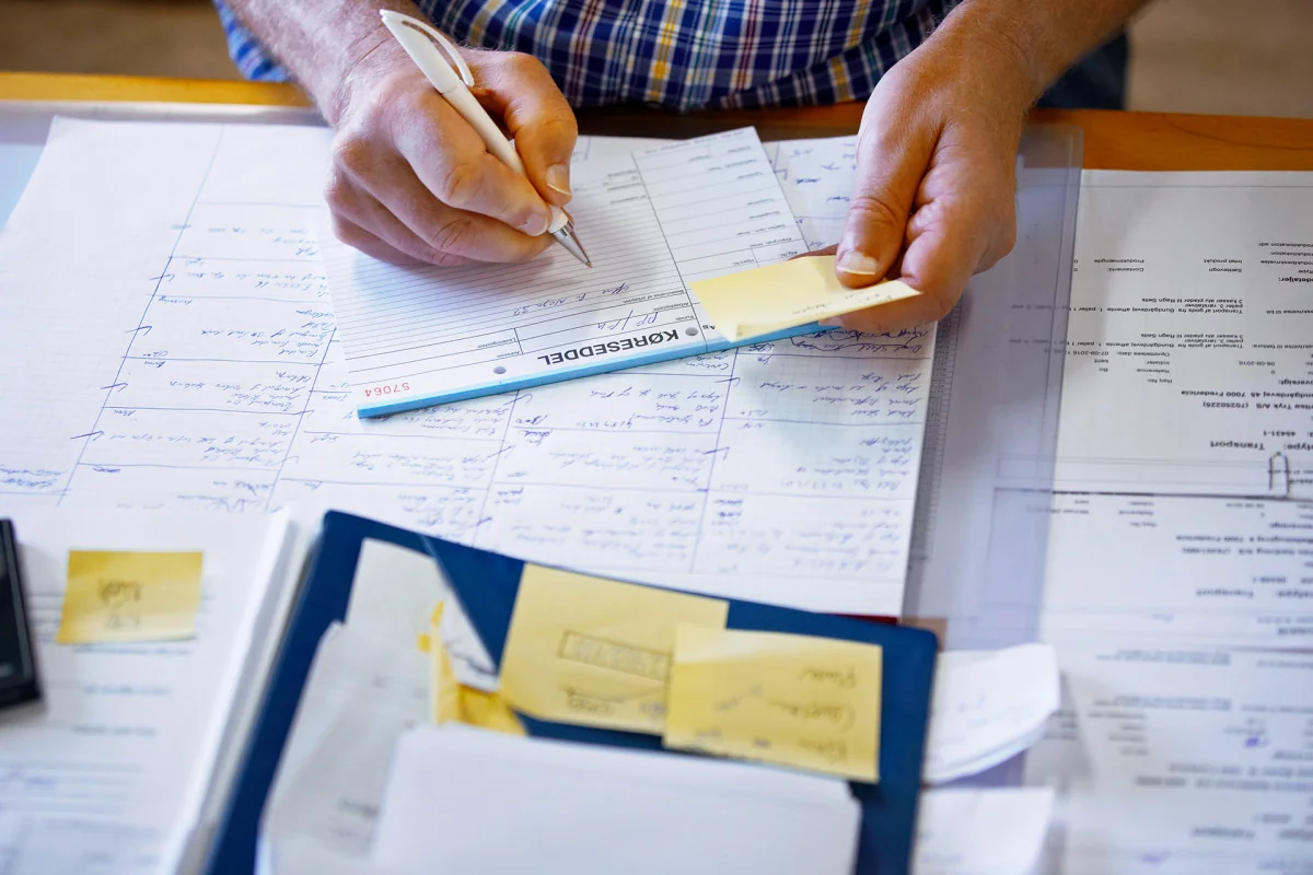 A person organizing paper documents and writing notes at a desk