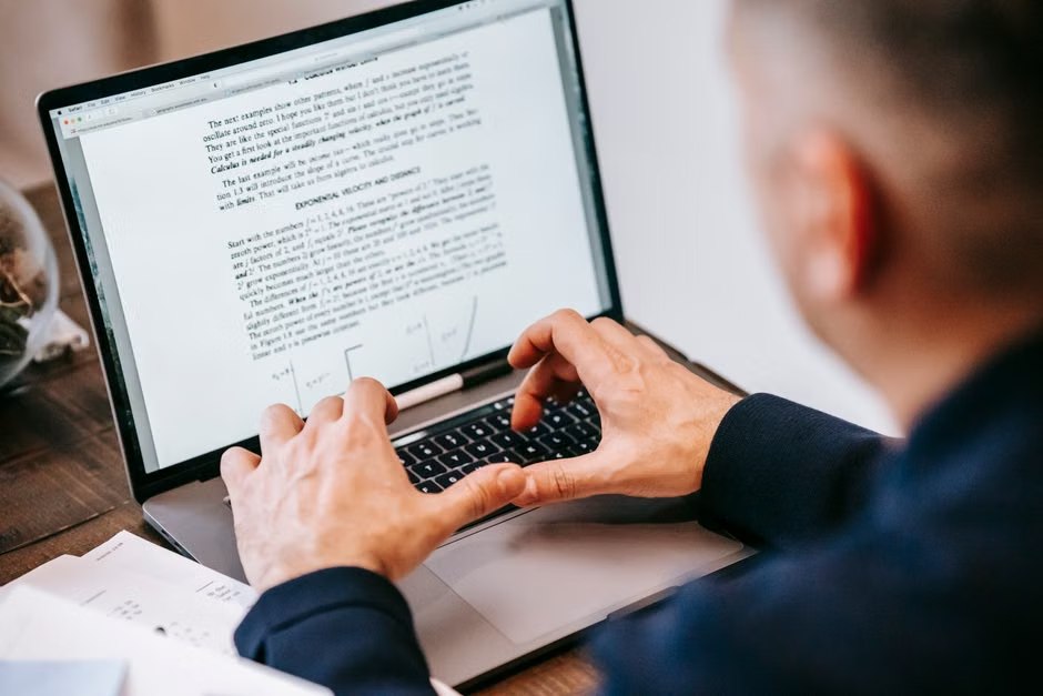 A person reviewing a document on a laptop beside printed pages