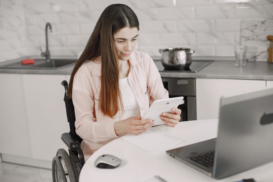 A woman using a tablet at a desk beside an open laptop